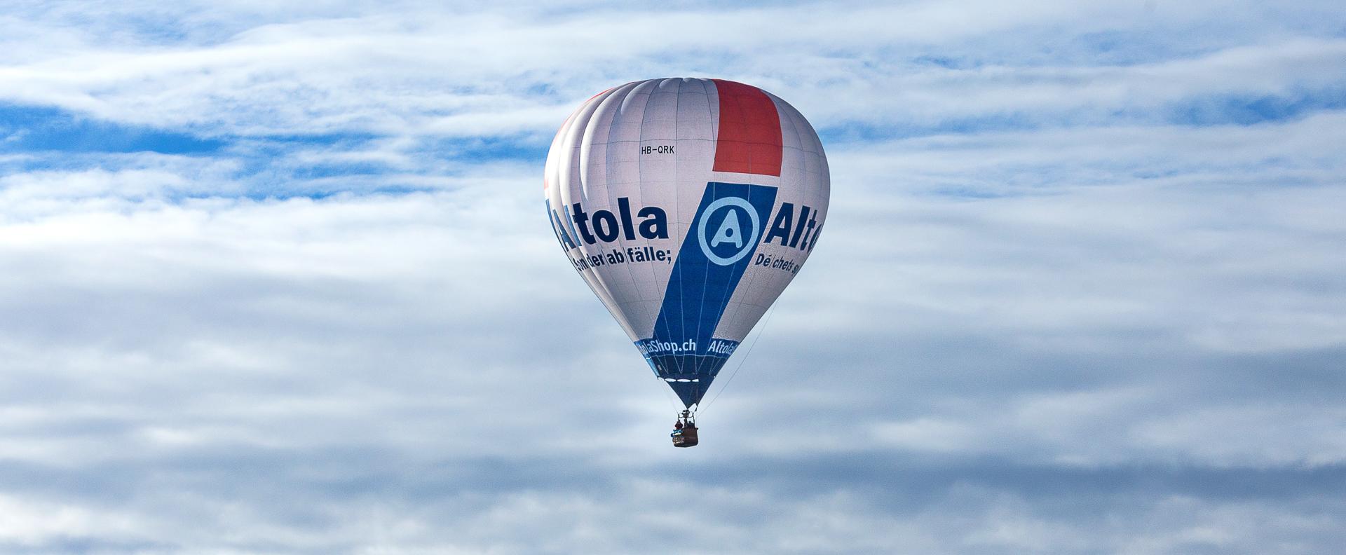 Ein weisser Heissluftballon am schweizer Himmel. Die Beschriftung ist von der Entsorgungsunternehmung Altola.