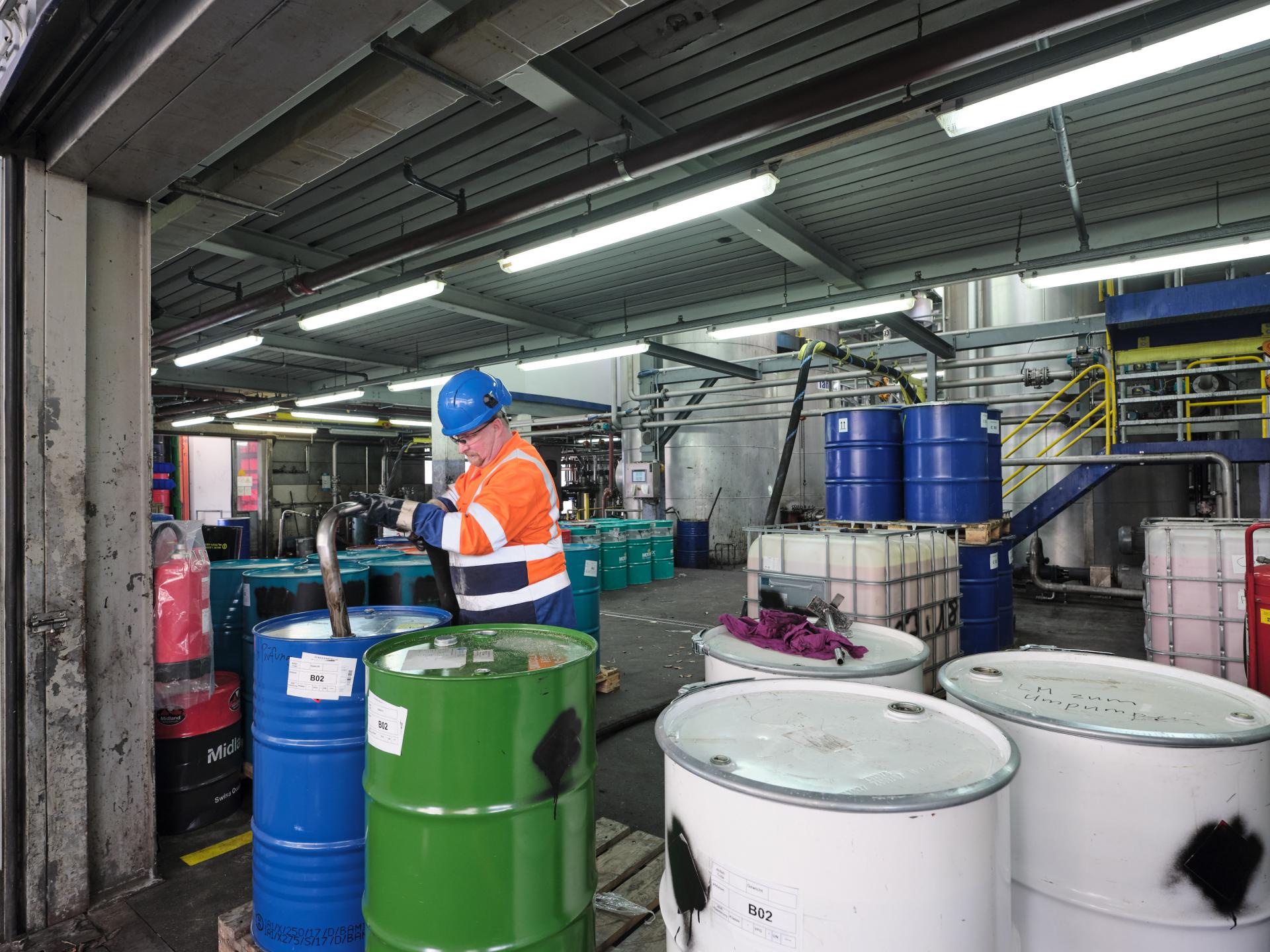 Ein Altola-Mitarbeiter in Sicherheitsausrüstung saugt ein Altölfass ab.