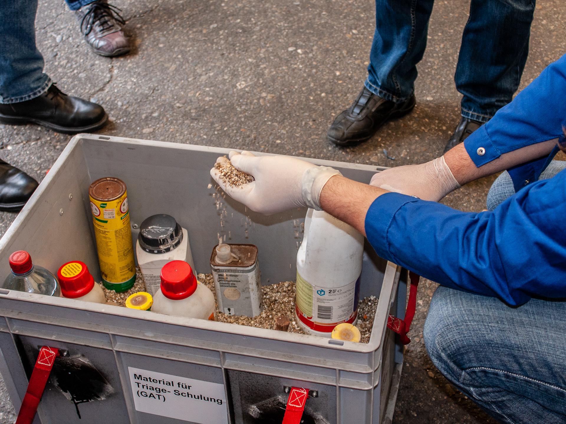 Eine graue Plastikbox. Darin stehen viele bunte Flaschen.