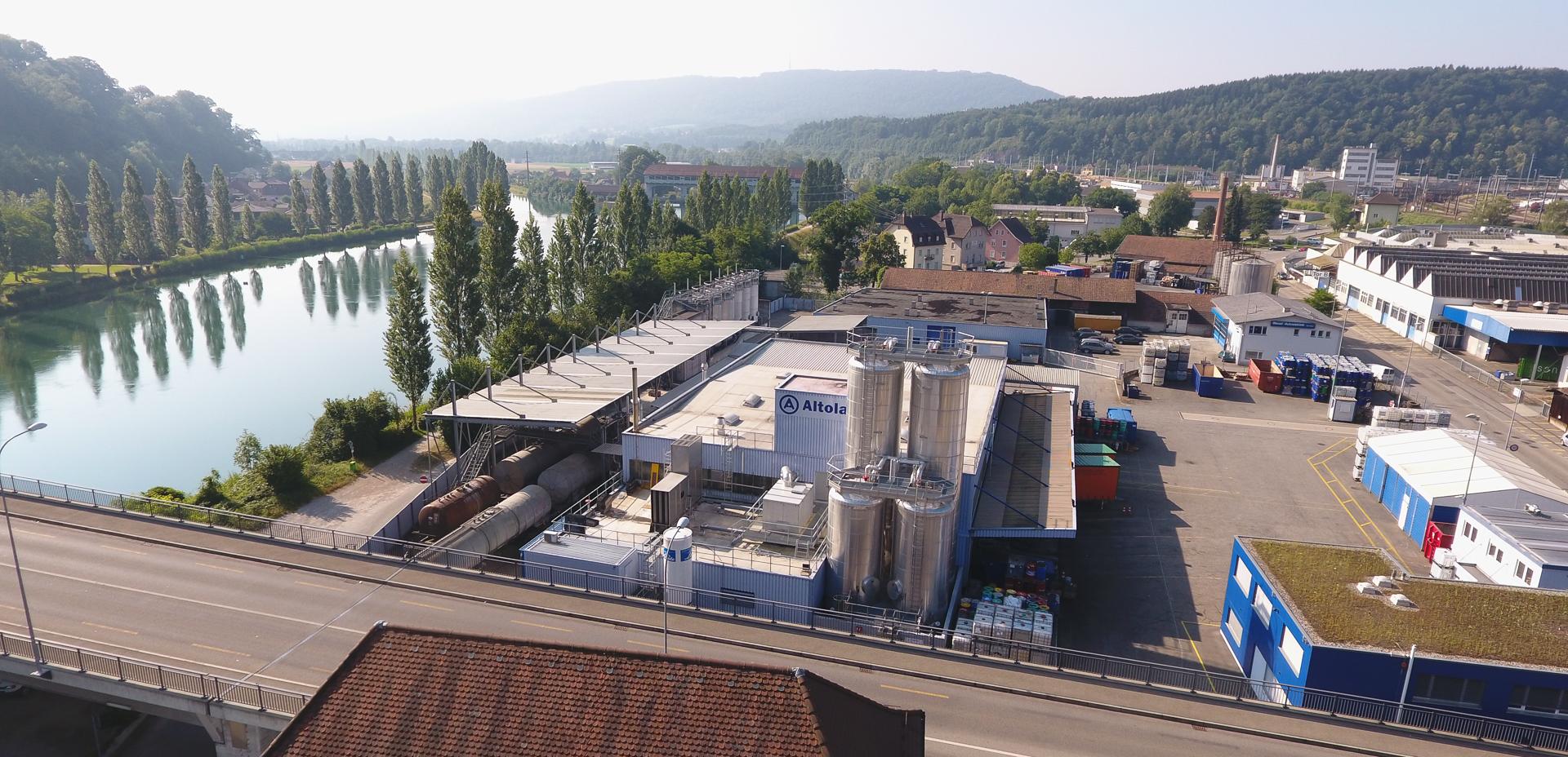 Der Altola-Standort in Olten liegt direkt an der Aare. Man sieht ein modernes Fabrikgebäude an einem sonnigen Tag.